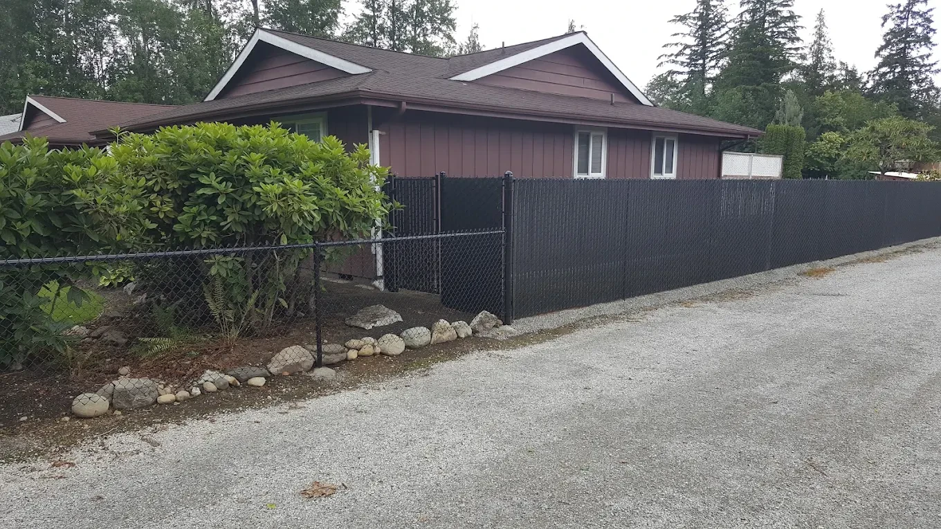 Black chain-link fence along modern house with forested backdrop